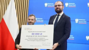 dwie osoby trzymające symboliczny czek, w tle flaga Polski